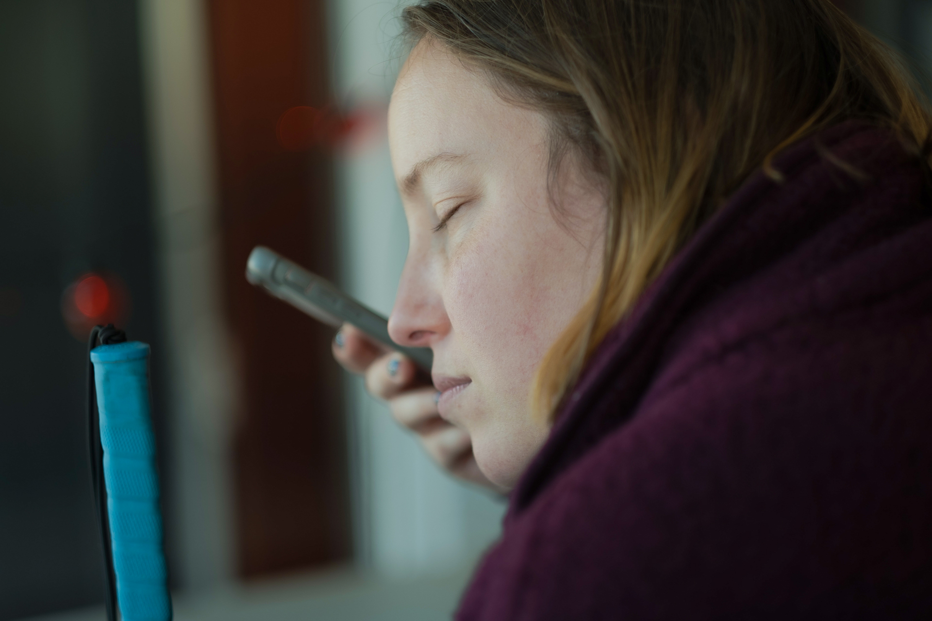 blind woman holding a mobile phone sitting at a desk.